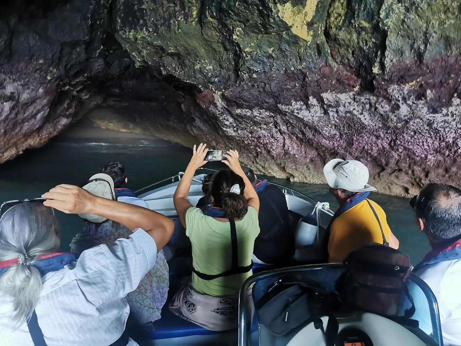 Passageiros no barco a fotografar uma gruta verde e roxa