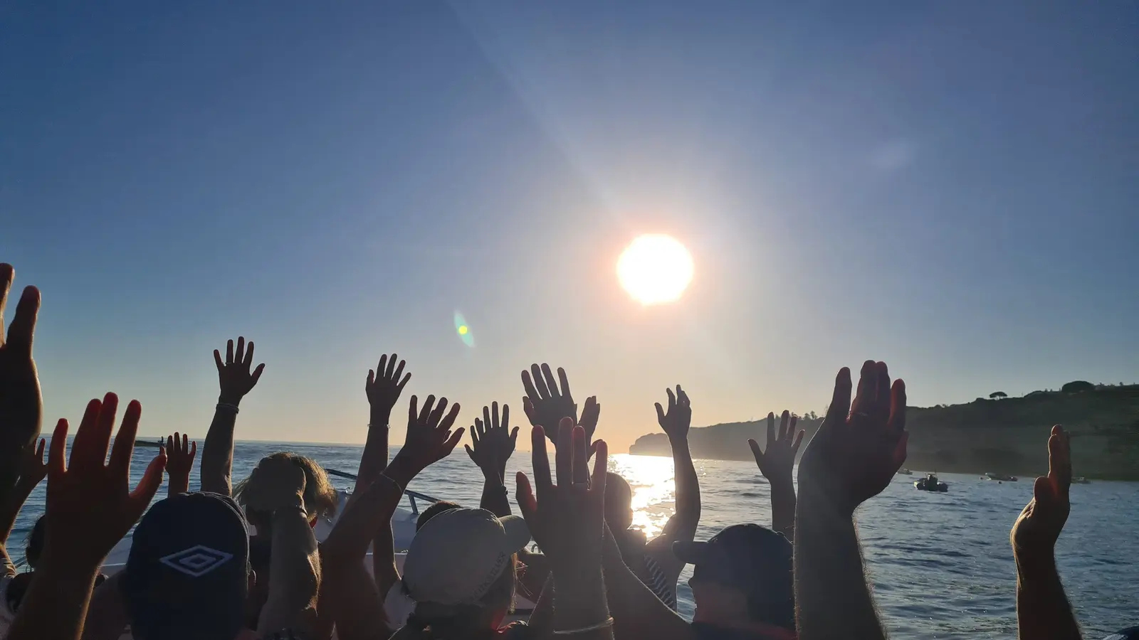 Mãos de passageiros contra o sol baixo e a costa