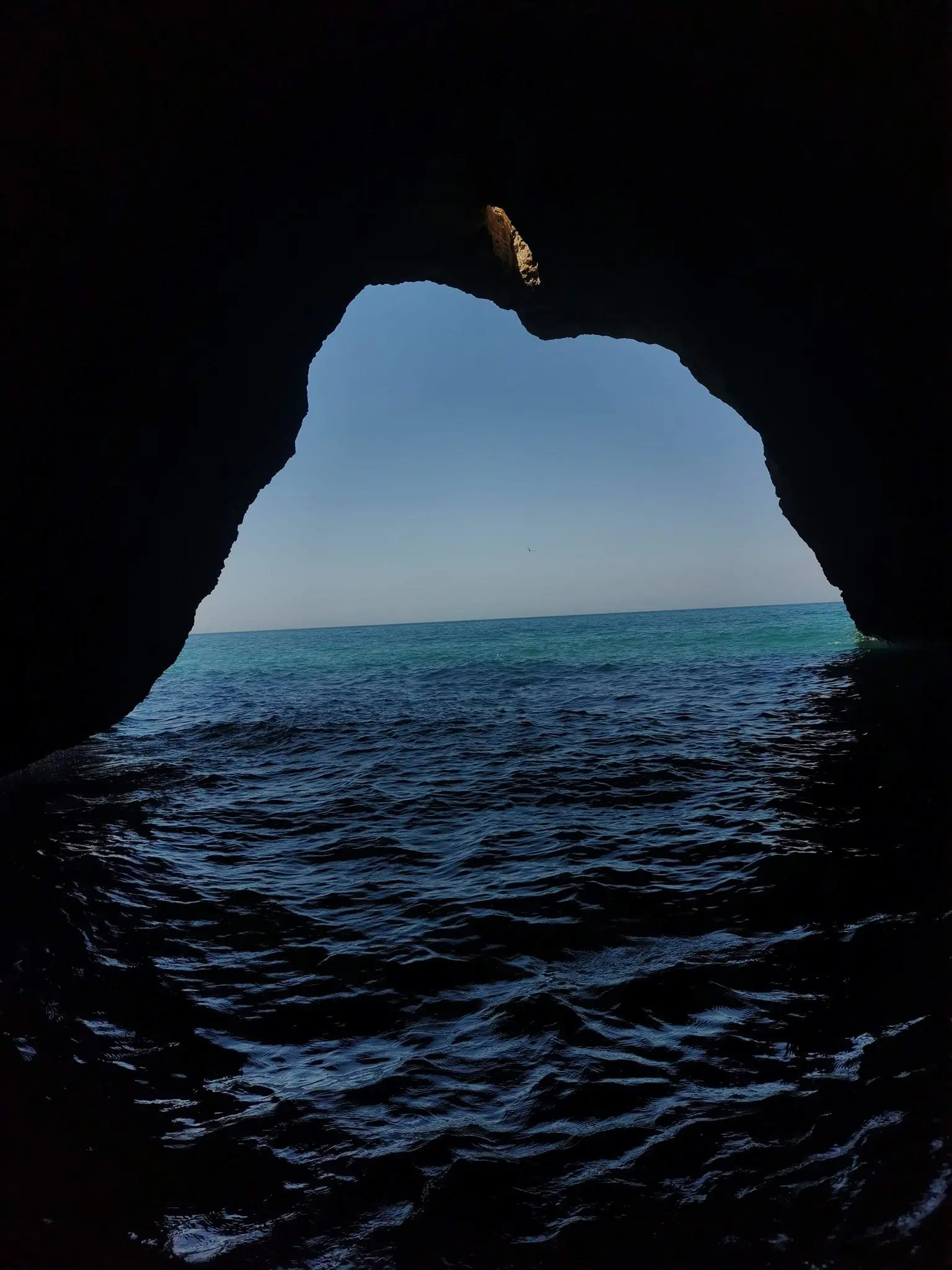 Boca escura de uma gruta a enquadrar o mar em forma de coração