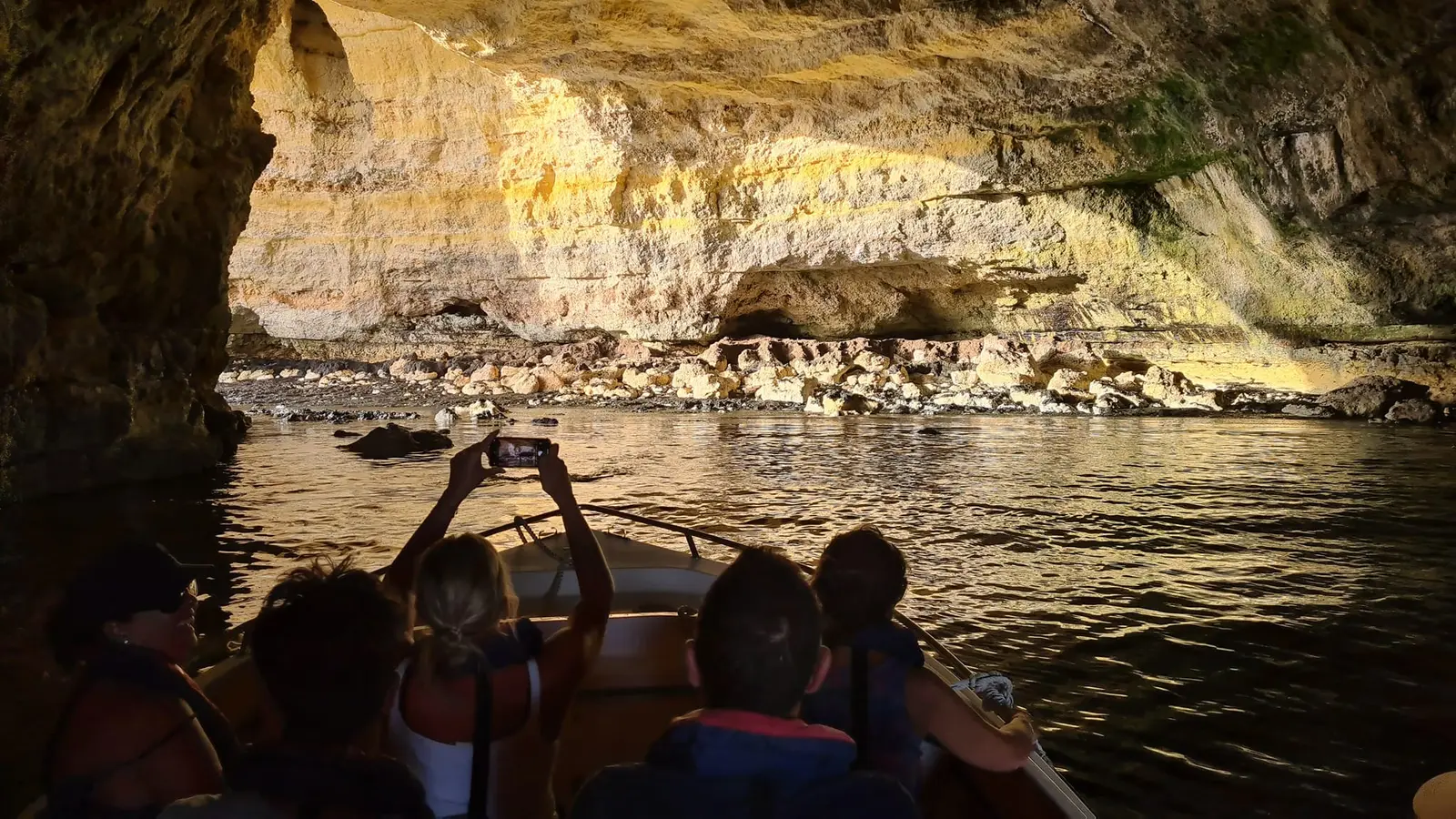 Silhuetas na proa a fotografar uma gruta ao fim da tarde