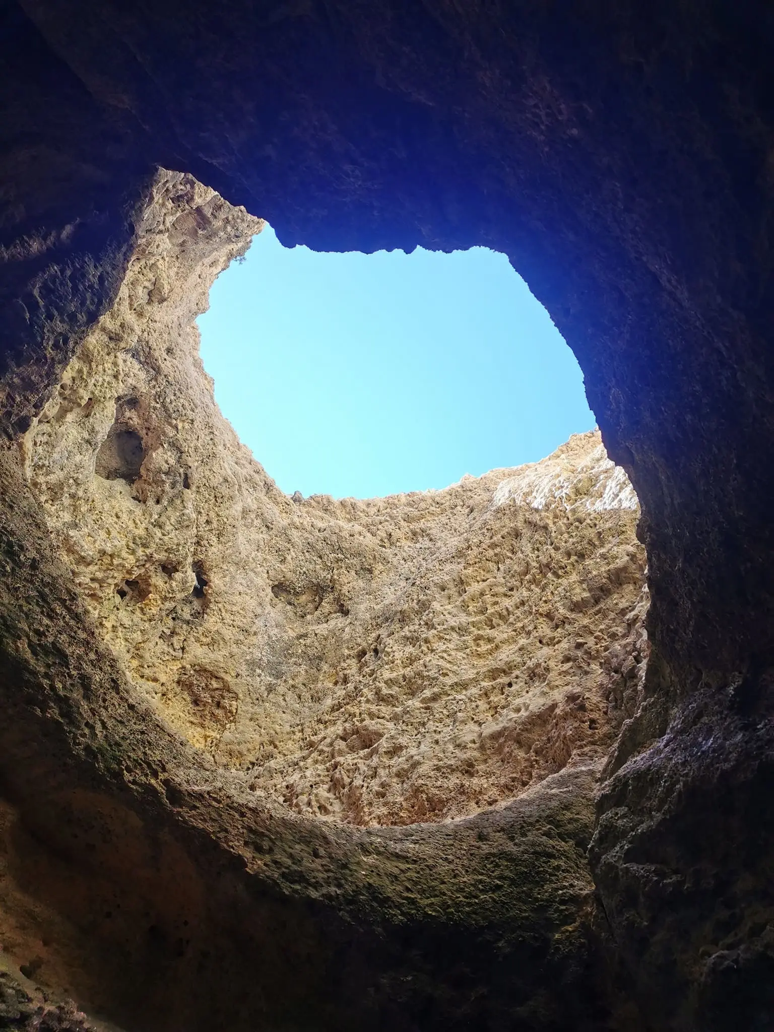 Abertura no teto de uma gruta, vista de baixo, com céu azul